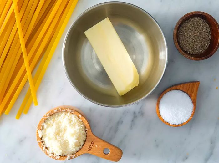 An aerial view of the ingredients for buttered noodles arranged in various sized bowls, with the noodles placed off to the side.