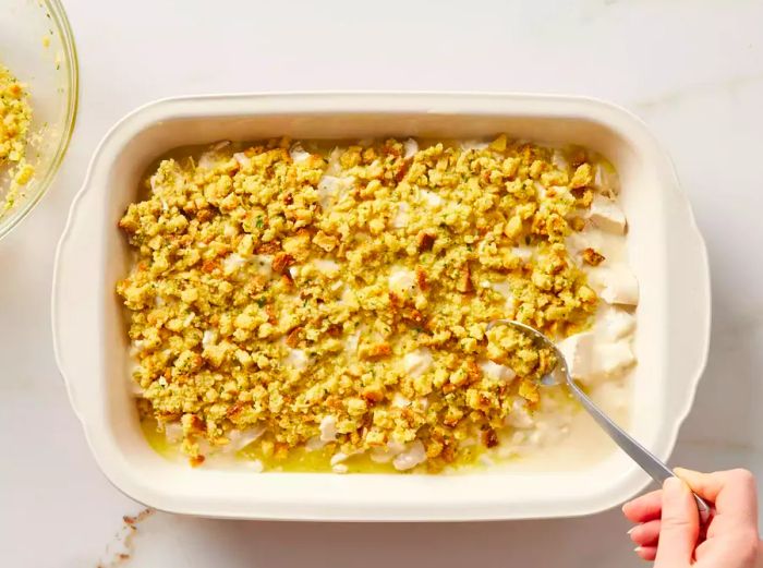 A spoon spreading a layer of stuffing over the soup and chicken casserole