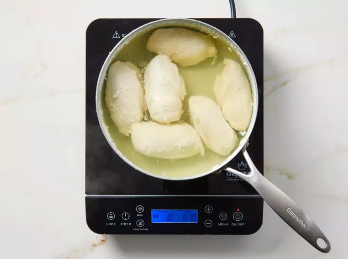 A pot with chicken cooking in simmering water