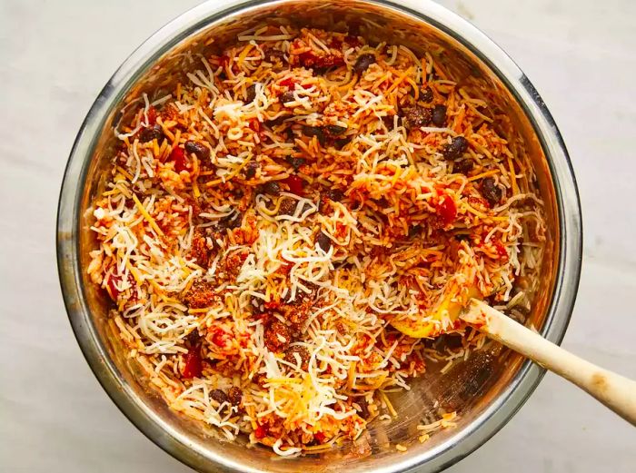 A top-down view of shredded cheese being mixed into a rice and tomato blend as it cooks in a pot. 