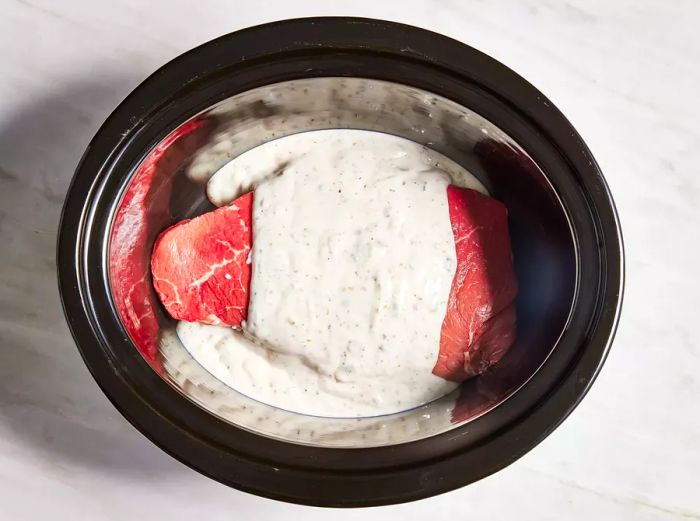 Garlic, herbs, condensed soup, and water added to a slow cooker with a London broil.