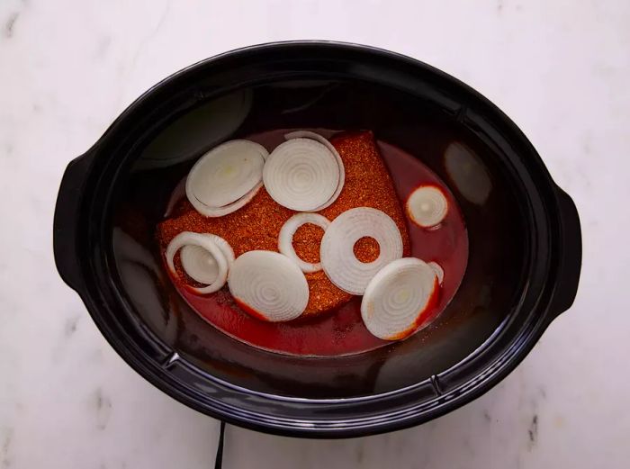 Once the barbecue sauce is spread at the bottom of the slow cooker, add the brisket and top it with onions.