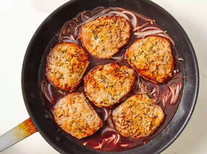 Red wine and beef consommé added to the skillet, with onions returned, cooking until the wine's aroma fades.