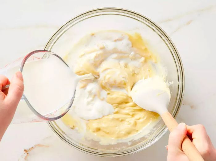 A hand pouring milk into a bowl of creamy condensed soup