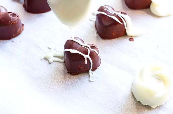 drizzling melted white chocolate over homemade dark chocolate candies