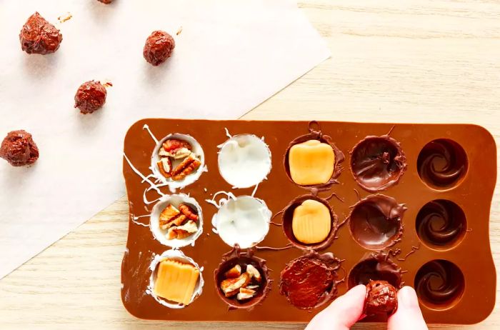 Add your choice of fillings, such as nuts, caramel, or chocolate truffles, to the chocolate-coated candy molds.