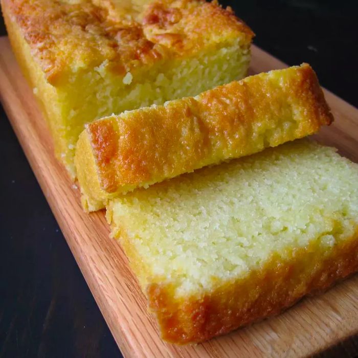 A high-angle view of a yogurt cake resting on a cutting board, with a few slices cut and ready to serve