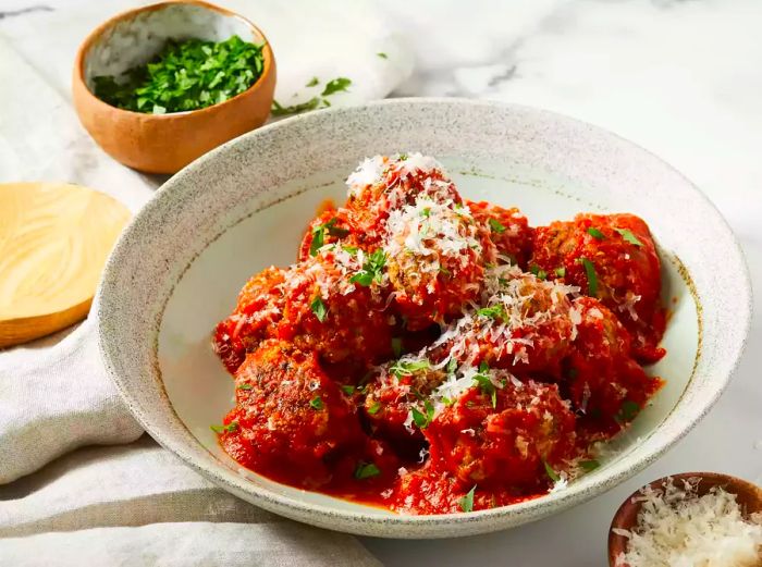 A close-up of a bowl of meatless meatballs in sauce, topped with grated cheese and fresh herbs.