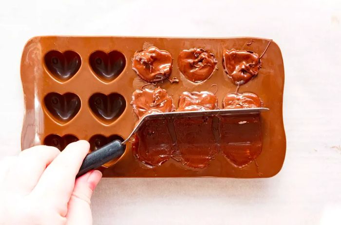 Using an offset spatula, scrape off any excess melted chocolate from the top of the filled molds