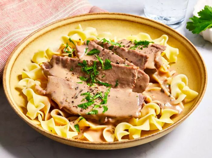 High-angle view of a bowl of egg noodles topped with slices of London broil and fresh herbs.