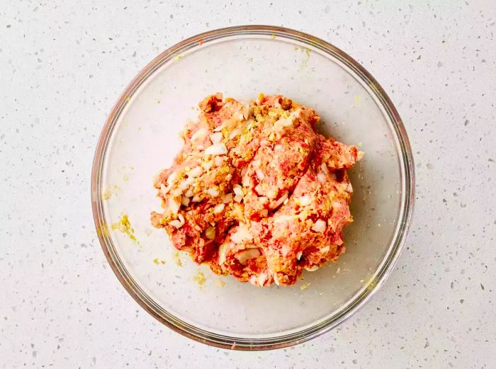 A glass bowl filled with the raw brown sugar meatloaf mixture, ready to be formed into a loaf.