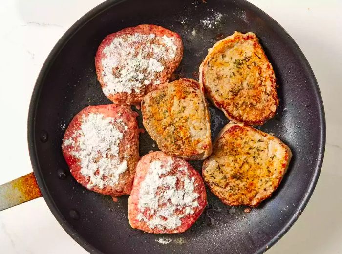 Steaks seasoned, dusted with flour, and frying until golden brown on both sides.