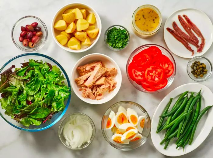 Various bowls and plates filled with ingredients for making Salad Niçoise.