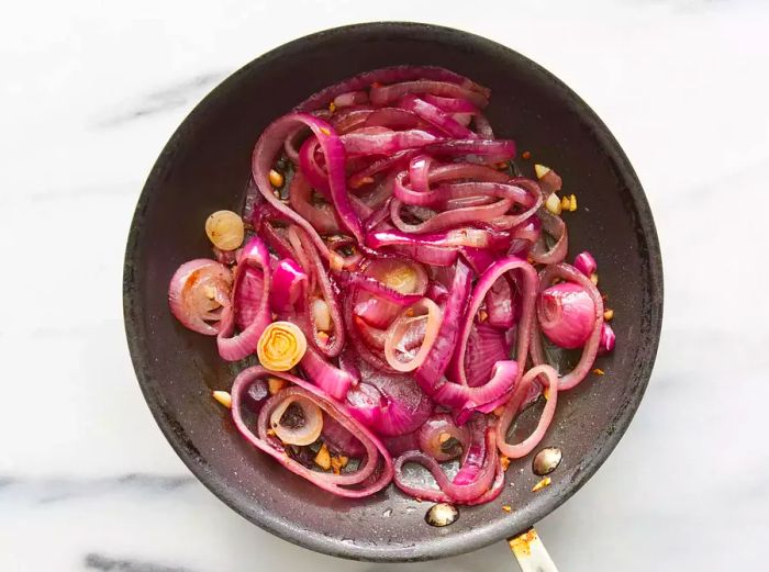 An aerial view of red onions sautéing in a skillet.