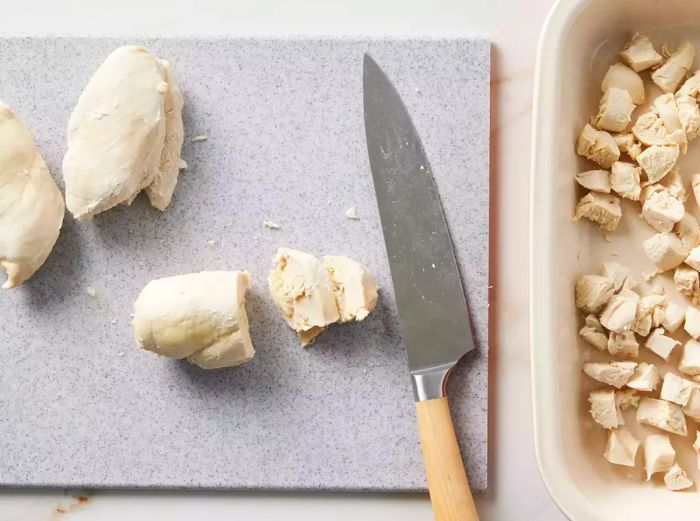 A cutting board with chopped chicken next to a baking dish filled with diced chicken