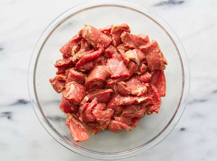 An aerial view of beef marinated in a mixture of lemon juice, soy sauce, sugar, salt, and pepper, all tossed together in a large bowl.