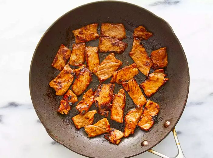 A top-down view of beef slices sizzling in oil in a skillet.