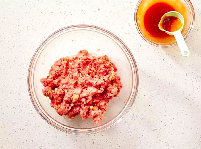 The meat mixture in a glass bowl, placed beside the ketchup glaze