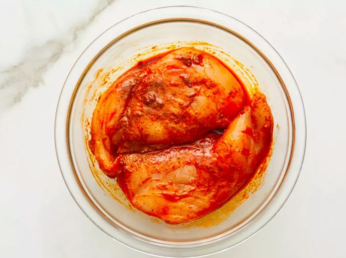 A top-down view of seasoned chicken breasts in a glass mixing bowl.