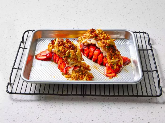 Crab-stuffed lobster tails resting on a baking sheet on a cooling rack