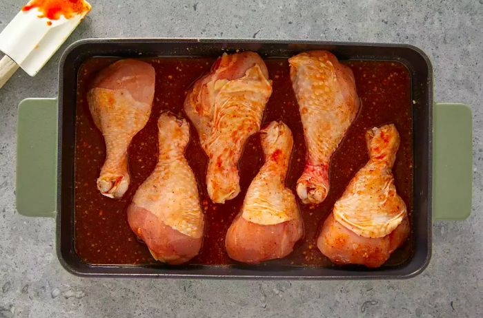 Five drumsticks coated in BBQ sauce and placed in a baking dish