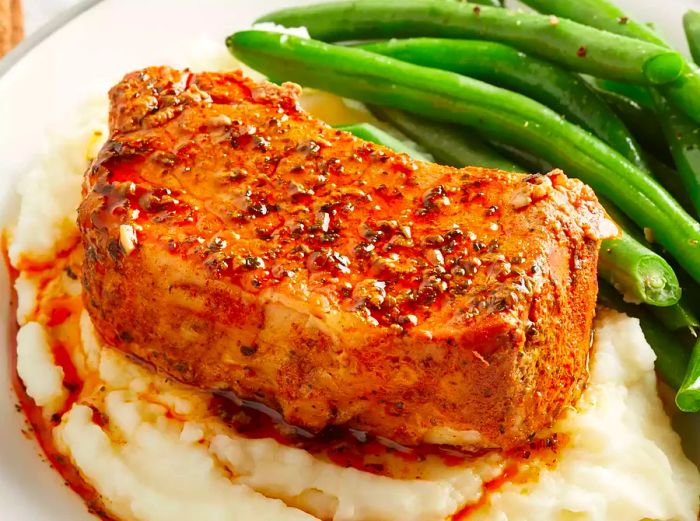 side view of slow-cooked pork chops atop mashed potatoes, served with green beans on the side