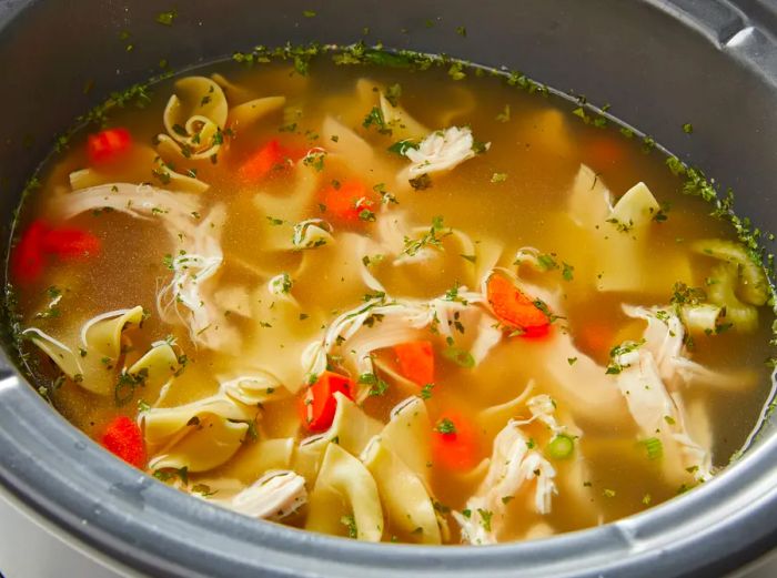 High-angle view into a slow cooker filled with chicken noodle soup.