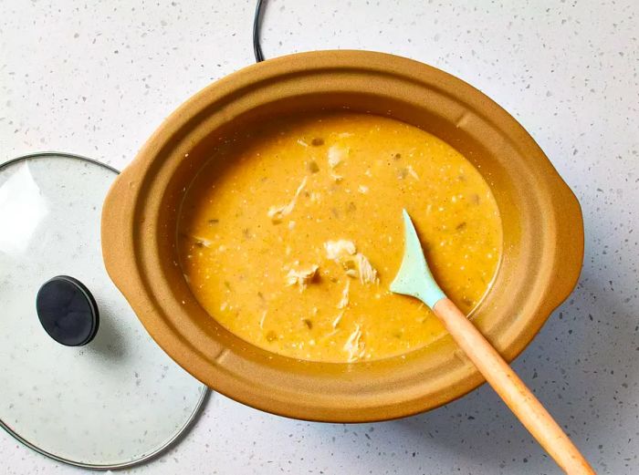 A slow cooker with white chicken chili being stirred with a silicone spatula.