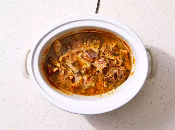 A slow cooker with fully cooked pork neck bones.