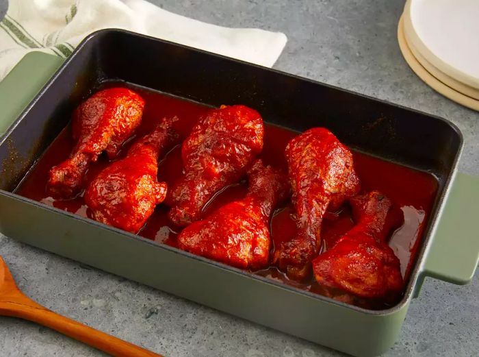 Close-up shot of six BBQ drumsticks arranged in a green baking dish