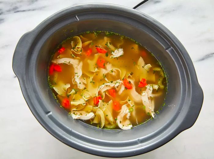 Aerial view of chicken noodle soup simmering in a slow cooker.