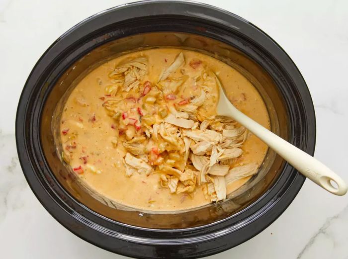 Shredded chicken and cream cheese being added back into the crockpot.