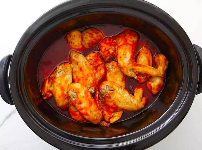 A bird's-eye view of chicken wings mixed with hot sauce in the slow cooker