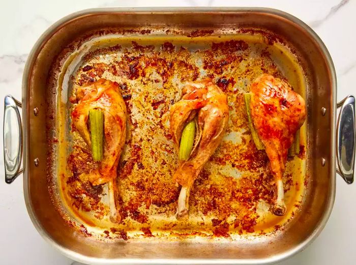 A bird's-eye view of three cooked turkey legs resting in a baking dish.