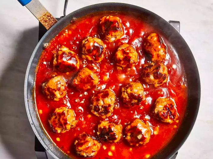 Meatballs simmering in a skillet with a rich, bubbling red sauce.