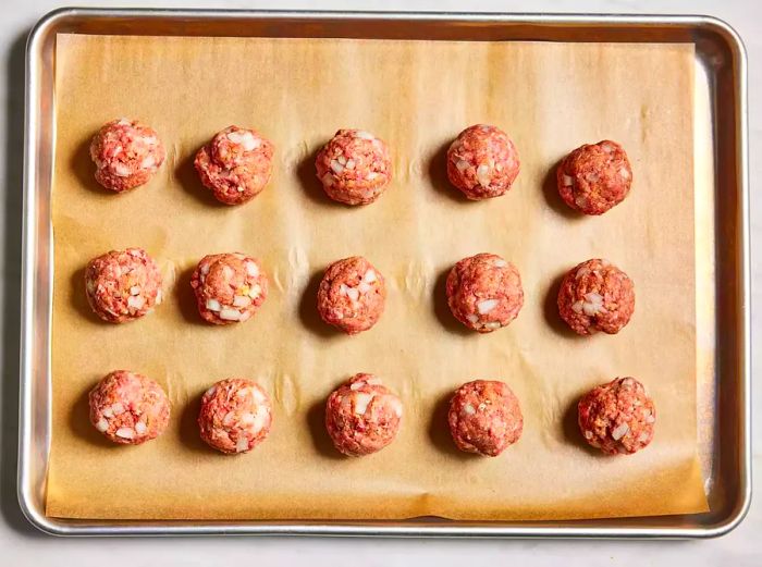 Aerial view of uncooked meatballs arranged on a baking sheet lined with parchment paper.