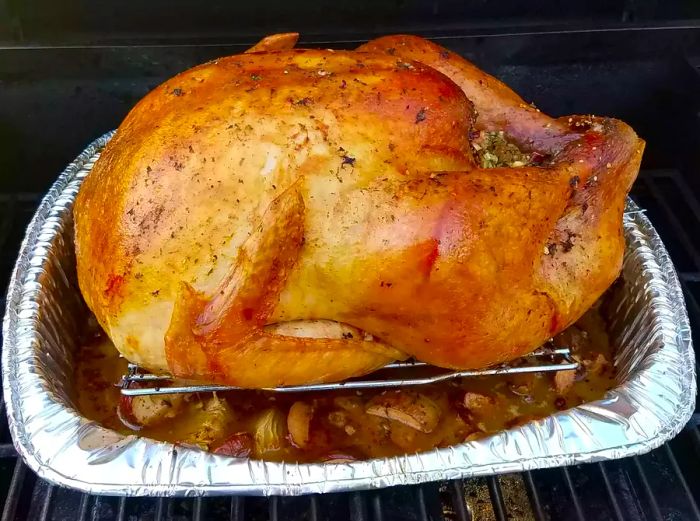A close-up of Grilled Turkey in an aluminum roasting pan, resting on the grill