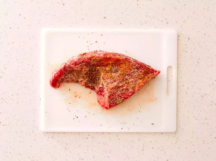 A tri-tip cut of beef, garnished with a blend of herbs and spices