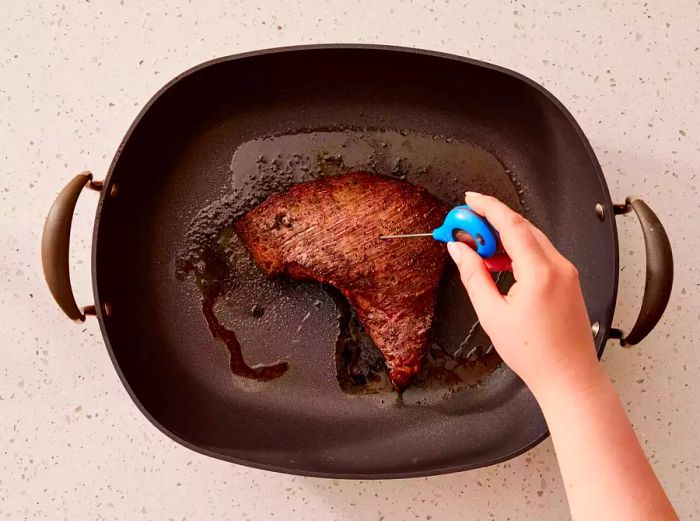 A roasting pan with a piece of perfectly cooked tri-tip beef, with a thermometer checking the doneness