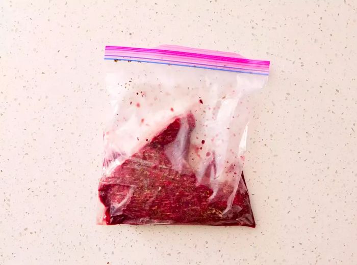 A zip-top plastic bag containing a seasoned beef tri-tip and red wine