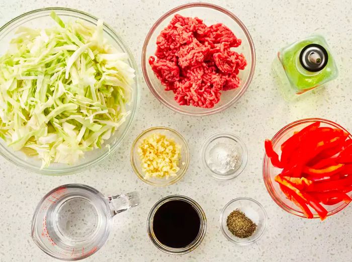 Aerial shot of all the ingredients for peppery beef and cabbage, neatly arranged in small bowls and measuring cups on a kitchen counter.