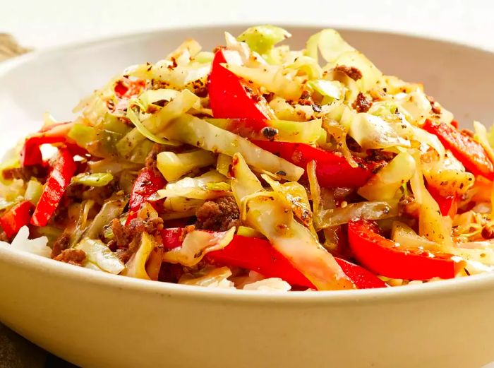 A close-up, eye-level shot of a bowl filled with black pepper beef, cabbage, and red peppers.