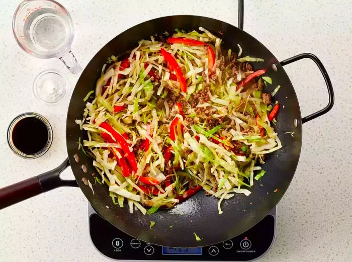 An overhead view of ground beef and cabbage being cooked until the vegetables soften and the beef is completely cooked in a hot wok.