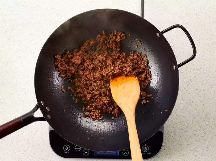 An aerial view of garlic and ground beef sizzling in a hot wok.