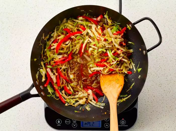 A cornstarch mixture being stirred into a hot wok of tender vegetables and cooked ground beef.