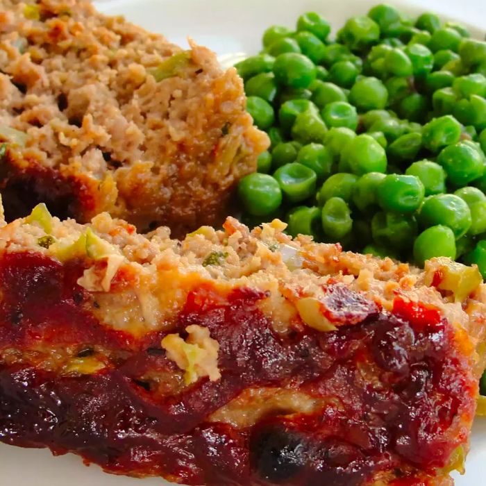 A close-up shot of sliced Zucchini Ranch Meatloaf served with green peas on a plate.