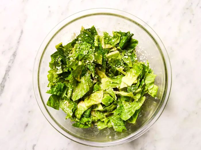 Romaine lettuce and Parmesan cheese tossed together in the dressing bowl.