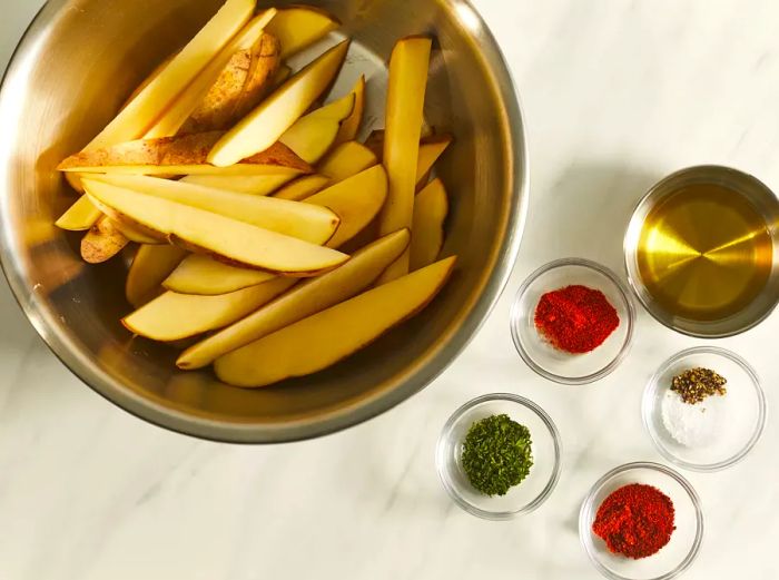 An overhead shot showing a bowl of potato wedges surrounded by small bowls of seasonings.