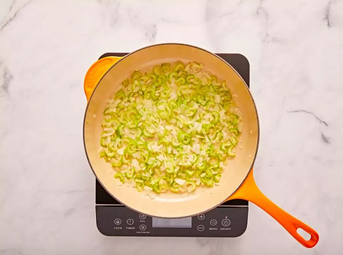 A top-down view of celery and onion sautéing in a pan.