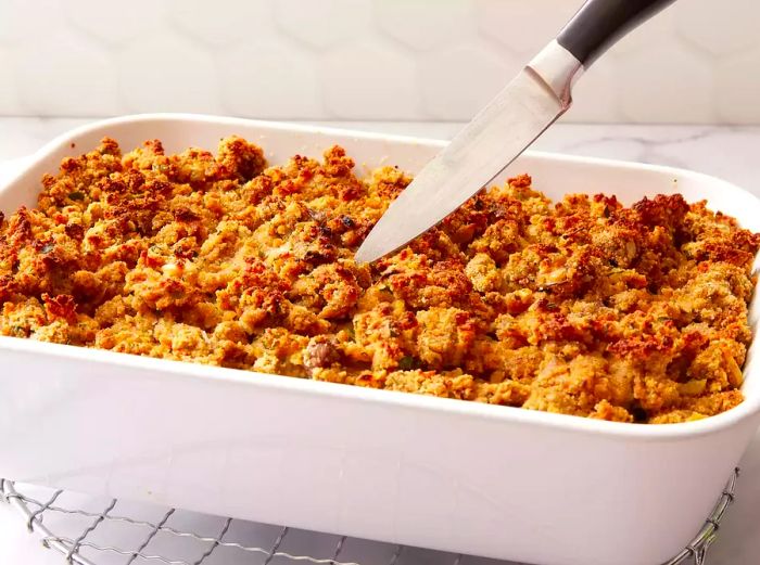 A side view of the oyster dressing in the baking dish with a knife resting on a cooling rack.